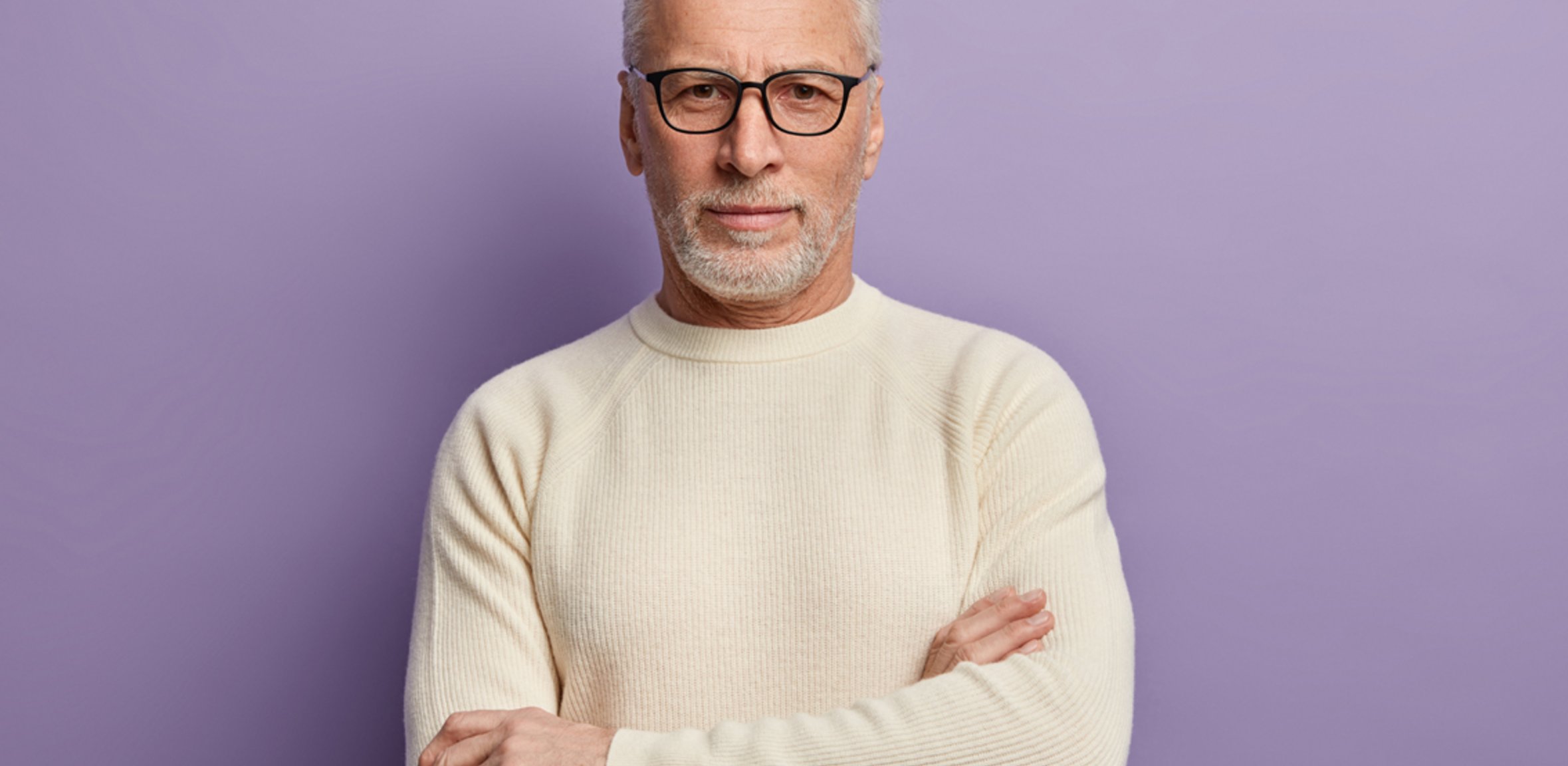 Mann mit grauem Haar und beigem Pullover vor lila Hintergrund