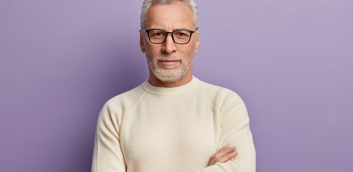 Mann mit grauem Haar und beigem Pullover vor lila Hintergrund